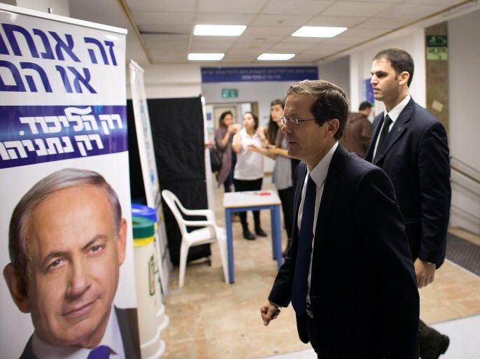 Isaac Herzog (C), co-leader of the Zionist Union party, walks past a Likud party campaign poster, that depicts Israeli Prime Minister Benjamin Netanyahu, as he arrives to address college students in Jerusalem March 10, 2015. REUTERS/Ronen Zvulun/File Photo