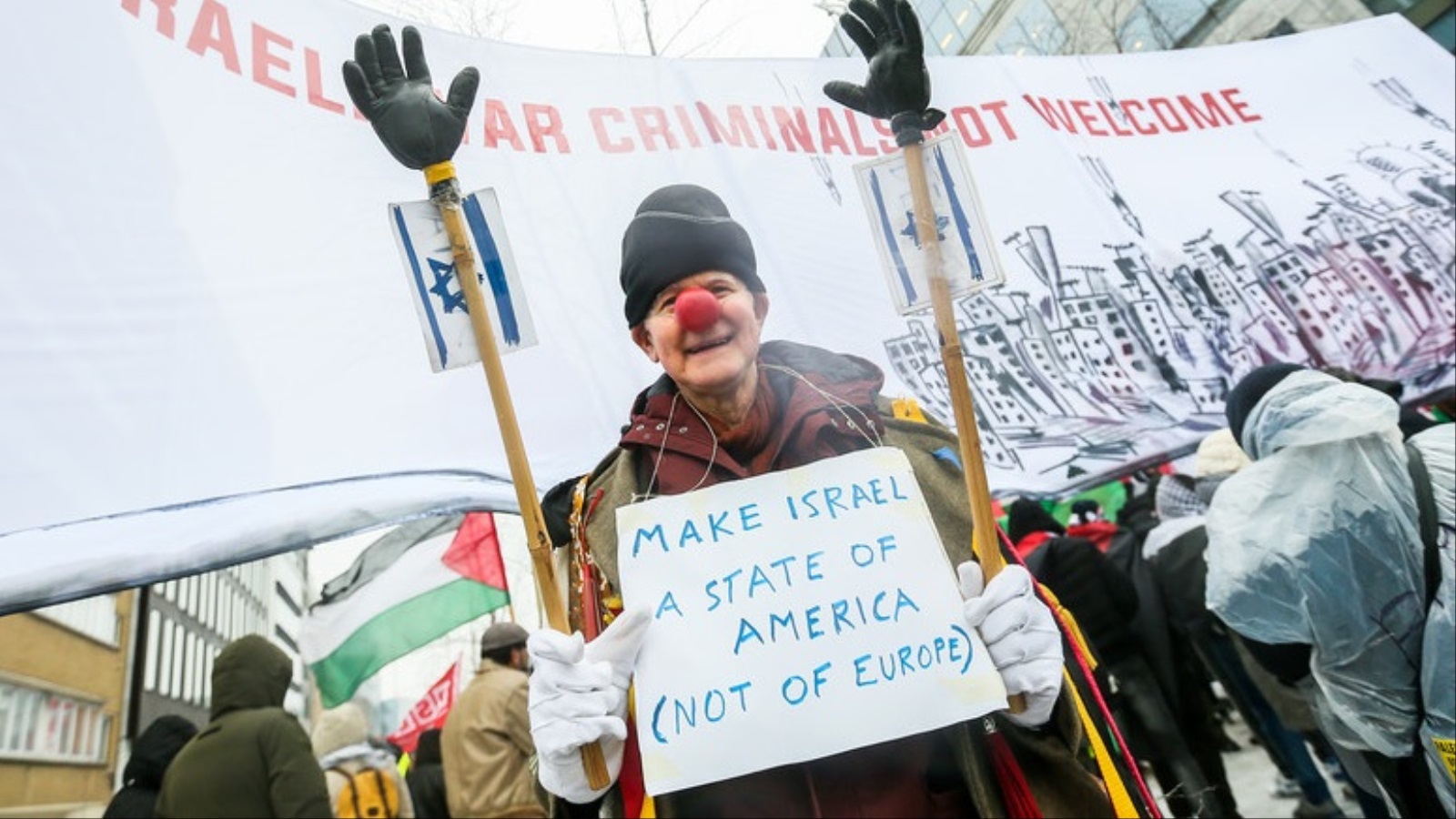 أحد المحتجين على زيارة نتنياهو لبروكسل يرفع لافتة تدعو لإلحاق إسرائيل بأميركا بدلا من إلحاقها بأوروبا (الأوروبية)