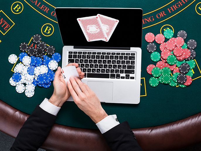 casino, online gambling, technology and people concept - close up of poker player with playing cards, laptop and chips at green casino table. top view. in the hands of two aces, a winning combination