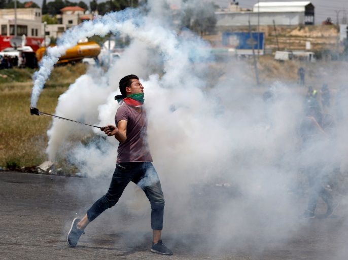 A Palestinian demonstrator uses a sling to hurl back a tear gas canister fired by Israeli troops during a protest marking the 70th anniversary of Nakba, near the Jewish settlement of Beit El, near Ramallah, in the occupied West Bank May 15, 2018. REUTERS/Mohamad Torokman