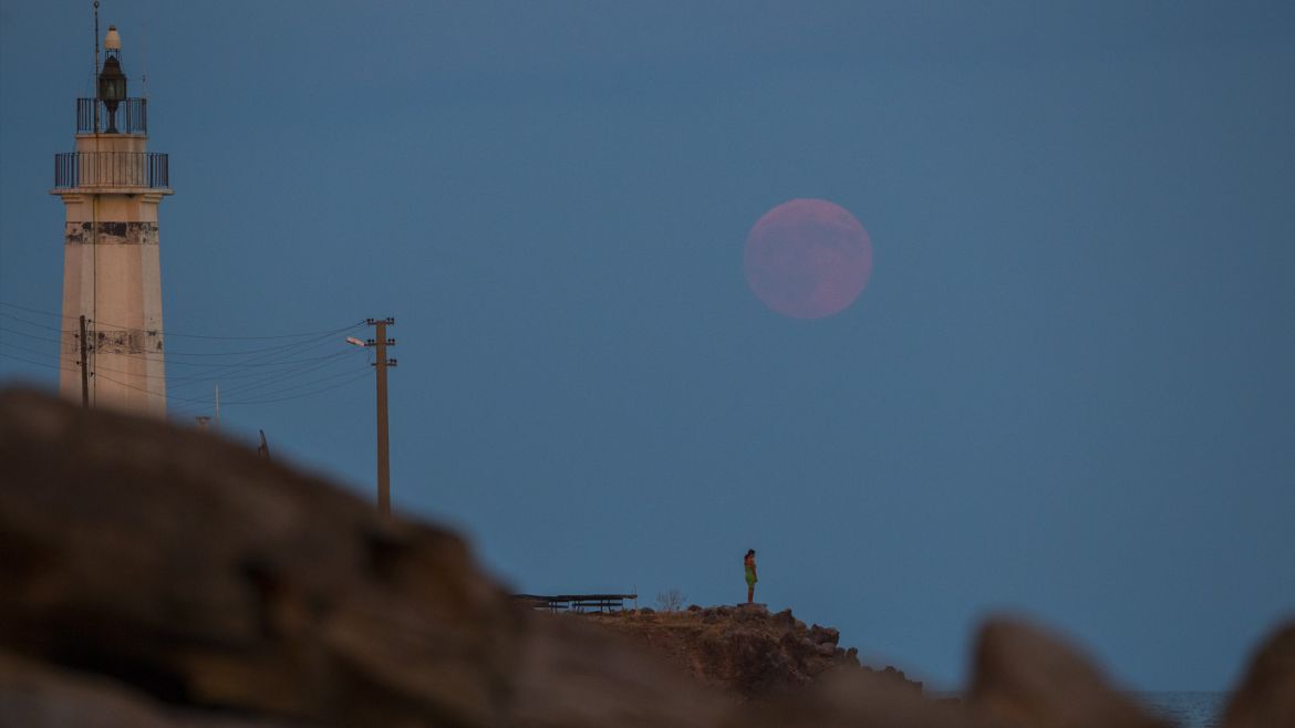 epa06914590 A woman watches full moon near a lighthouse at Sivrice village in Canakkale city, Agean coast of Turkey, 27 July 2018. The lunar eclipse of the night of 27 July 2017 will be the longest total lunar eclipse of the 21st century with the event spanning for over four hours, and the total eclipse phase lasting for 103 minutes. EPA-EFE/TOLGA BOZOGLU