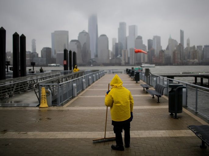 A ferry worker cleans the path for commuters during light snowfall while the New York skyline and the One World Trade Center are seen from Exchange Place in New Jersey, U.S., March 7, 2018. REUTERS/Eduardo Munoz
