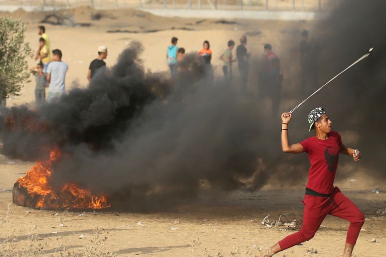 A Palestinian hurls stones at Israeli troops during a protest calling for lifting the Israeli blockade on Gaza and demanding the right to return to their homeland, at the Israel-Gaza border fence in the southern Gaza Strip October 19, 2018. REUTERS/Ibraheem Abu Mustafa