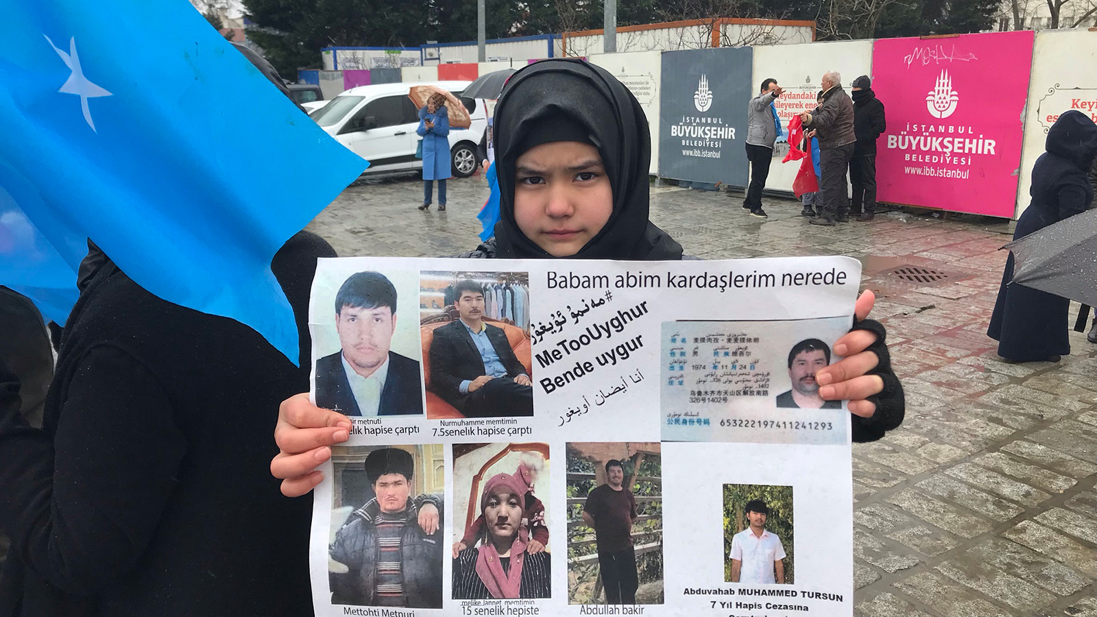 طفلة من الإيغور ترفع صور أقارب لها في مسيرة التنديد بإجراءات الصين في إقليم تركستان الشرقية (الجزيرة)