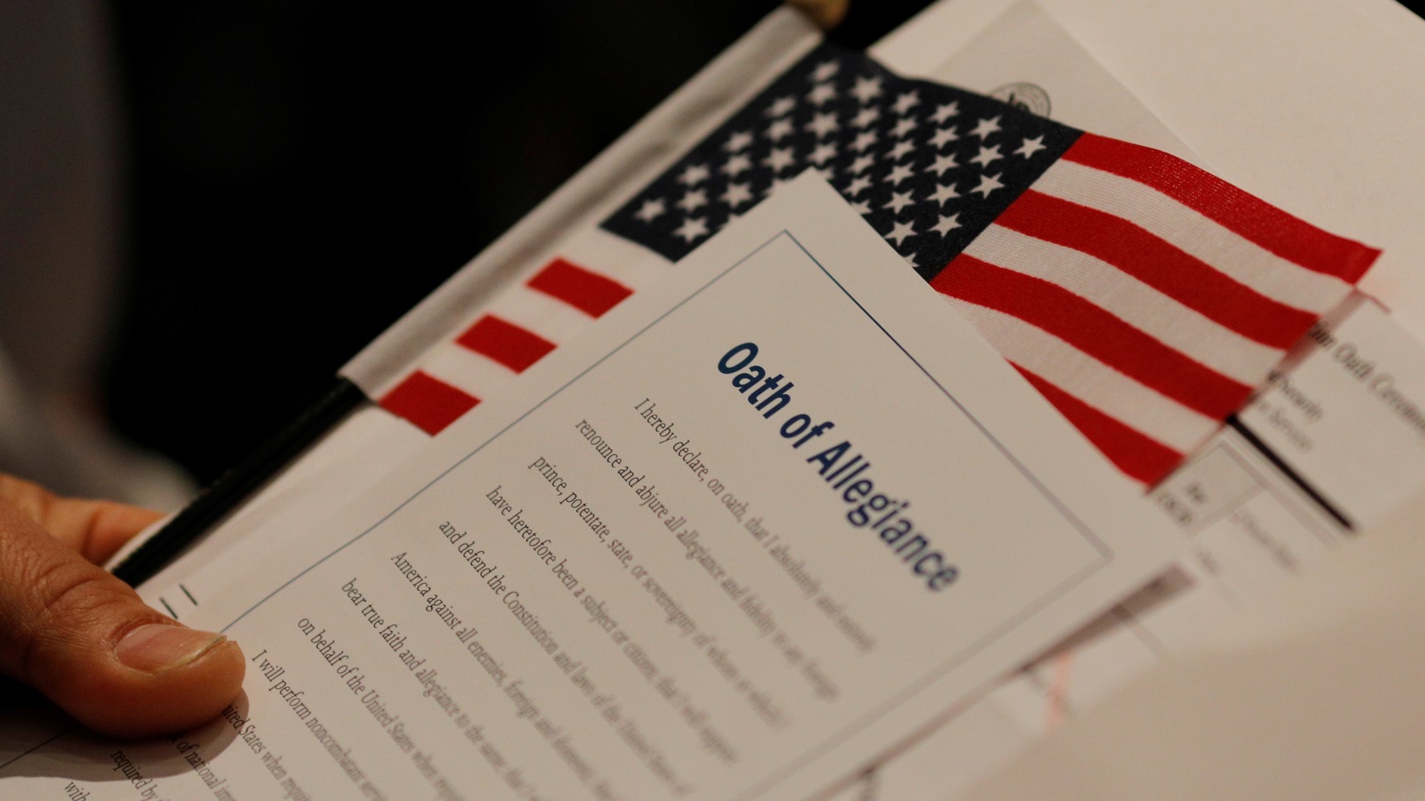‪مواطن أميركي جديد يحمل علم بلاده وورقة كتبت عليها كلمات القسم الذي يؤديه كل من يحصل على الجنسية الأميركية‬ (رويترز)