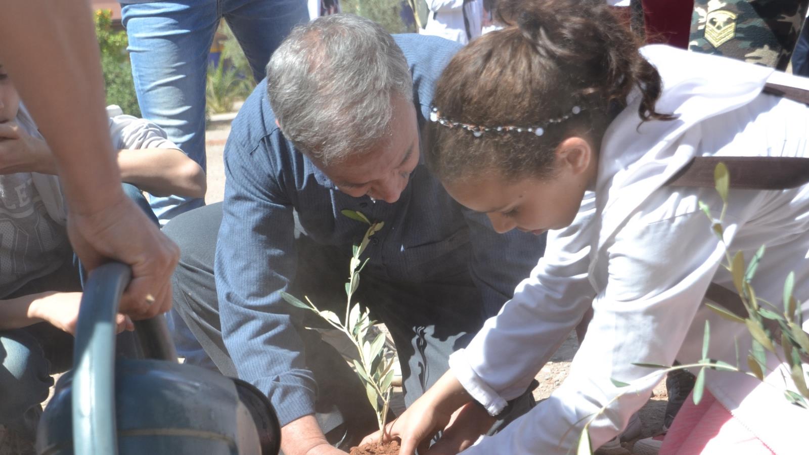 ‪أستاذ العلوم النباتية يساعد تلميذة في زرع شجرة تكفلت بها‬ (الجزيرة)