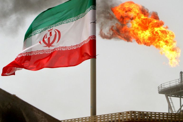 A gas flare on an oil production platform in the Soroush oil fields is seen alongside an Iranian flag in the Persian Gulf, Iran, July 25, 2005. REUTERS/Raheb Homavandi/File Photo