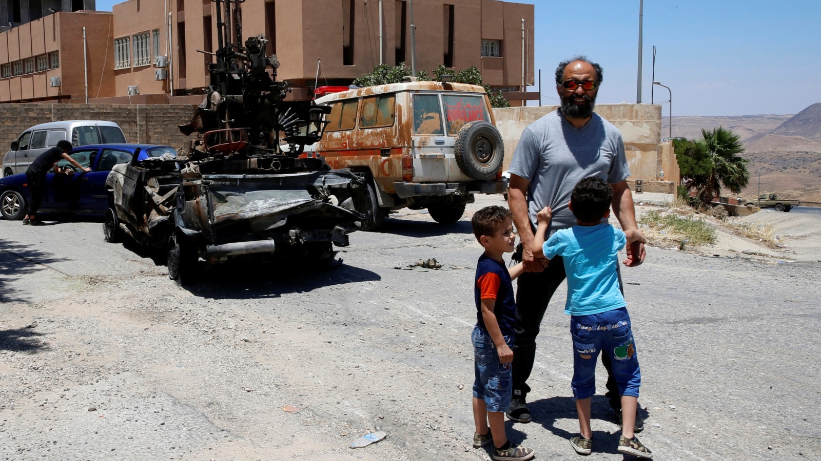‪أب وطفلاه قرب مركبة عسكرية مدمرة تابعة لقوات حفتر بأحد شوارع غريان‬  (رويترز)