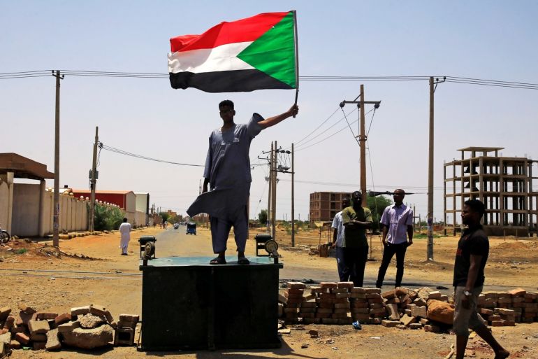 A Sudanese protester holds a national flag as he stands on a barricade along a street demanding that the country's Transitional Military Council hand over power to civilians in Khartoum Sudan June 5 2019. REUTERS/Stringer