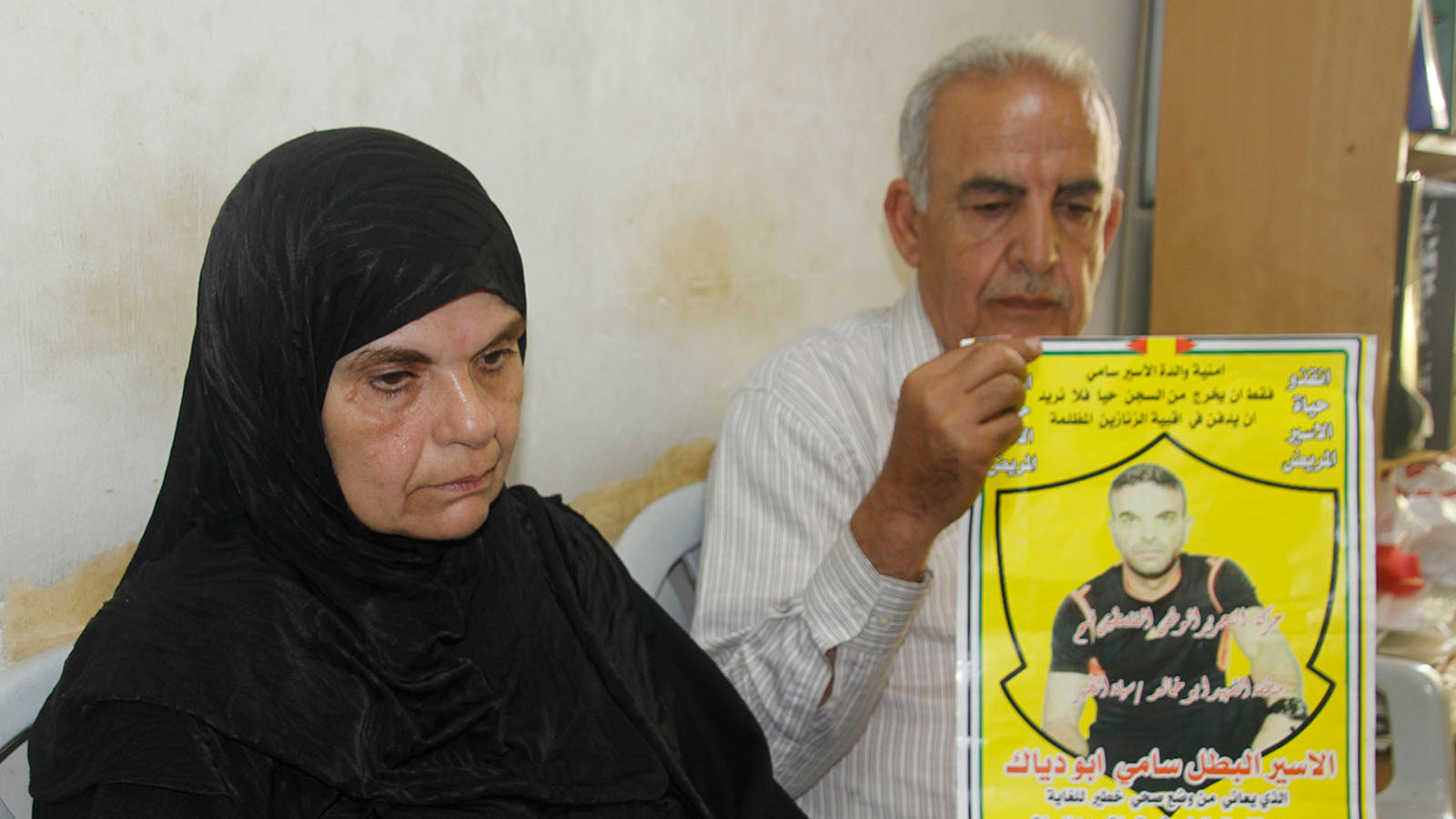 والد الأسير سامي أبو دياك ووالدته يحملان وصوره ويتوقعان استشهاده بأي لحظة  (الجزيرة)