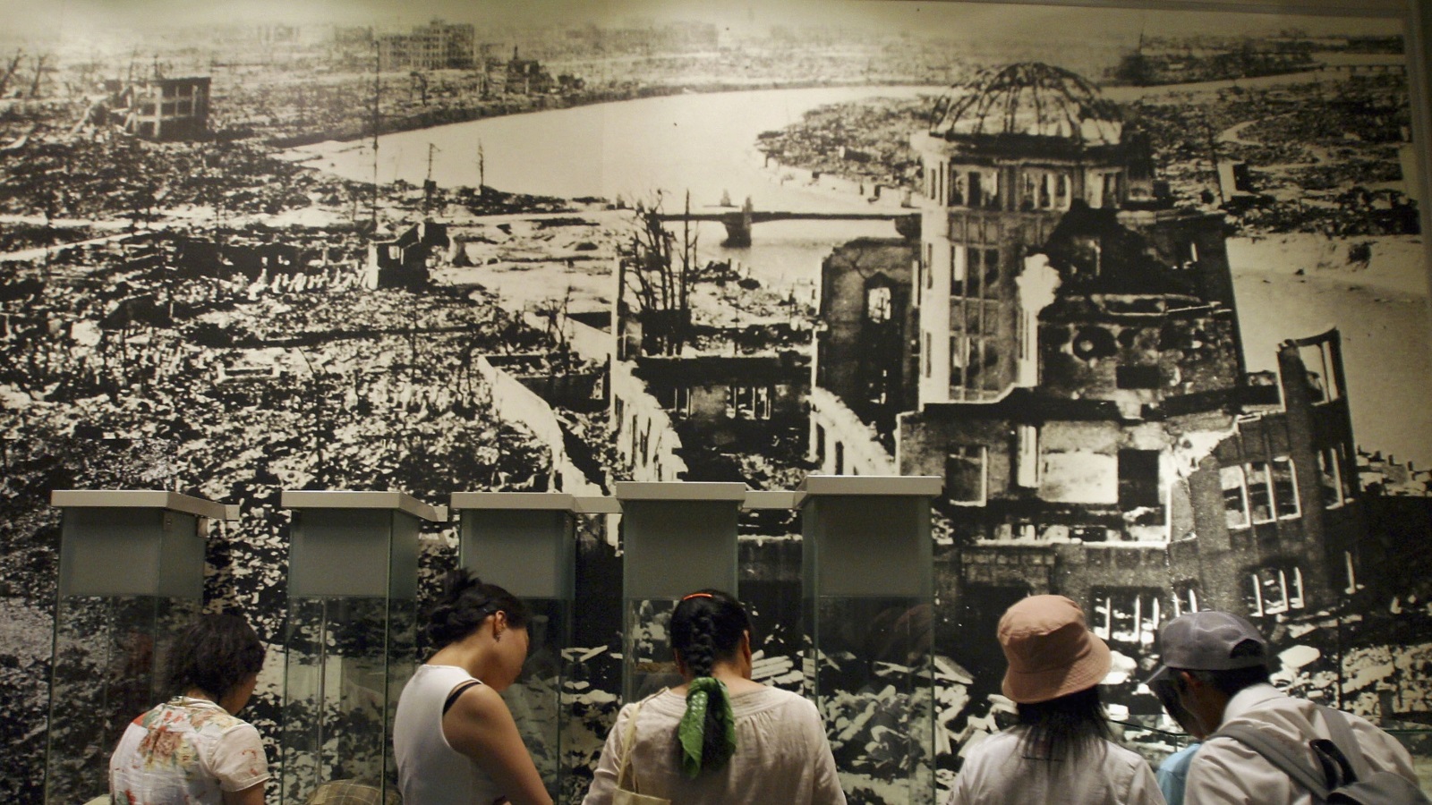 ‪أشخاص يتفحصون ملصقا لصورة التقطت لمكان سقوط القنبلة النووية على هيروشيما‬ (غيتي)