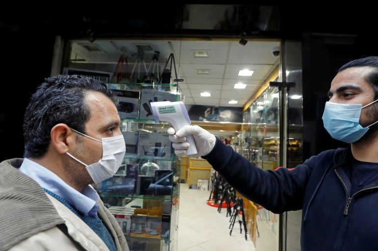 A shop assistant checks customers' temperature before they walk into the store, due to the coronavirus disease (COVID-19) outbreak, in Cairo, Egypt March 19, 2020. REUTERS/Mohamed Abd El Ghany