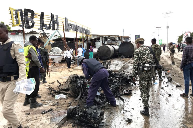 Somali security officers assess the wreckage of a car destroyed at the scene of an explosion in Mogadishu