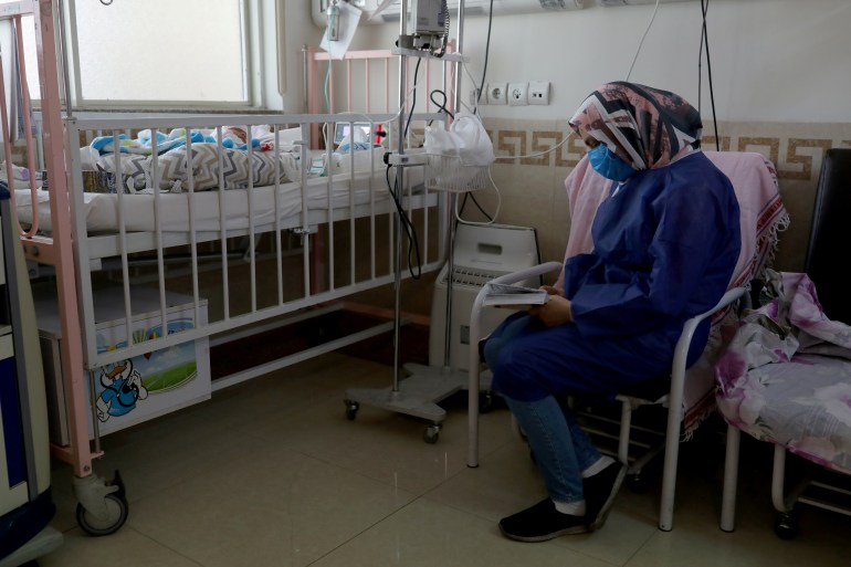 A mother wearing a protective suit and mask reads the Quran next to her baby who is affected by the coronavirus disease (COVID-19), at Hazrate Ali Asghar Hospital, in Tehran