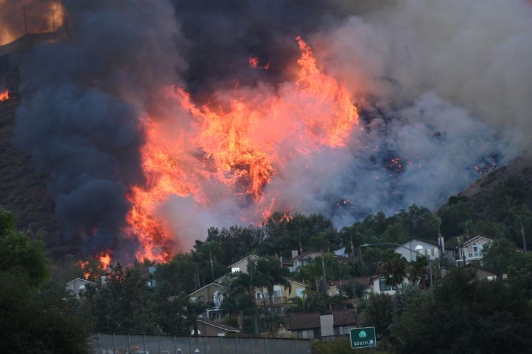 (FILES) In this file photo taken on October 27, 2020 Flames are seen near homes off the 71 freeway at the Blue Ridge Fire in Chino, California, October 27, 2020. - Two wind-driven wildfires in southern California continue their race toward populated areas, forcing 100,000 residents to evacuate and choking much of the region with smokey unhealthy air. (Photo by Robyn Beck / AFP)