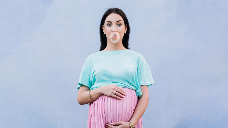 a pregnant stylish girl in a pink skirt and a mint T-shirt hugged her belly with both hands and blows a ball of gum on the background of the blue wall; Shutterstock ID 1038422593; purchase_order: ajnet; job: ; client: ; other: