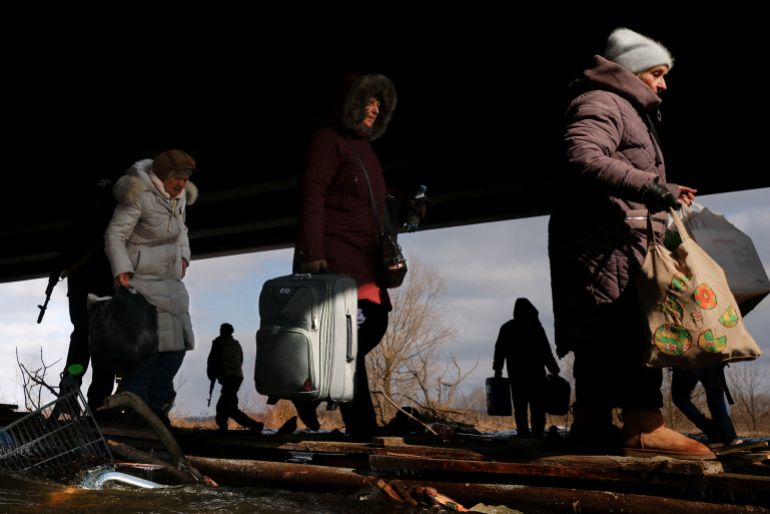People fleeing advancing Russian forces file across wooden planks crossing Irpin River below a destroyed bridge as Russia's attack on Ukraine continues in Irpin