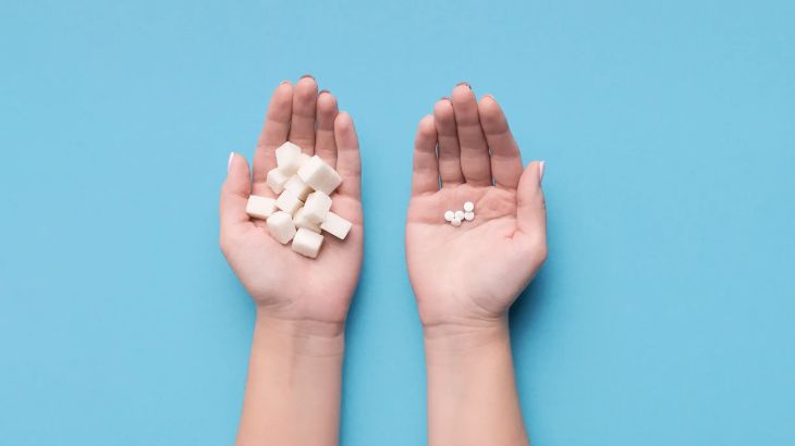 Female hands with sugar and pills on blue background. Choice of sweetener in tablets or regular sugar. Alternative to sugar for diabetics.
