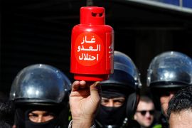 A demonstrator holds a mockup of a gas cylinder next to police officers during a protest against a government agreement to import natural gas from Israel, in Amman, Jordan, January 3, 2020. A sign on a model reads "The enemy's gas is occupation". REUTERS/Muhammad Hamed
