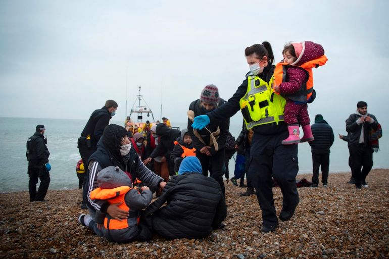 TOPSHOT-BRITAIN-FRANCE-EUROPE-MIGRANTS TOPSHOT - A member of the UK Border Force (R) helps child migrants on a beach in Dungeness, on the south-east coast of England, on November 24, 2021 after being rescued while crossing the English Channel. - The past three years have seen a significant rise in attempted Channel crossings by migrants, despite warnings of the dangers in the busy shipping lane between northern France and southern England, which is subject to strong currents and low temperatures. (Photo by Ben STANSALL / AFP) (Photo by BEN STANSALL/AFP via Getty Images)