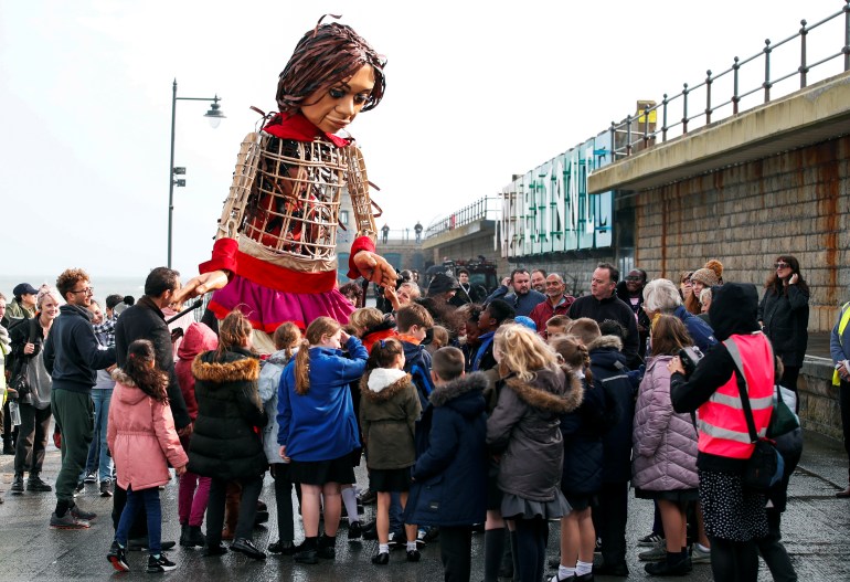 Children from St Mary's Primary Academy gather around 'Little Amal', a 3.5 metre tall puppet of a young Syrian refugee girl, as part of its 8.000 km tour across Europe from Turkey to Britain to raise awareness for the plight of young refugees, in Folkestone, Britain, October 19, 2021. REUTERS/Peter Cziborra