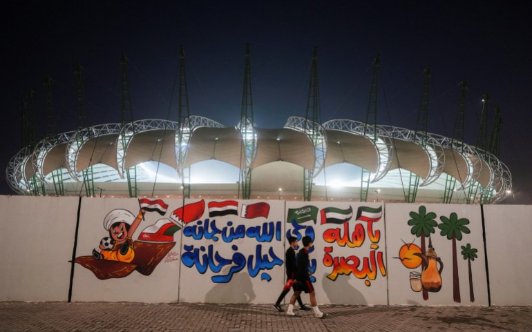 Iraqi men walk in front of Al-Minaa Olympic Stadium braces to host the Arabian Gulf Cup25, in Basra