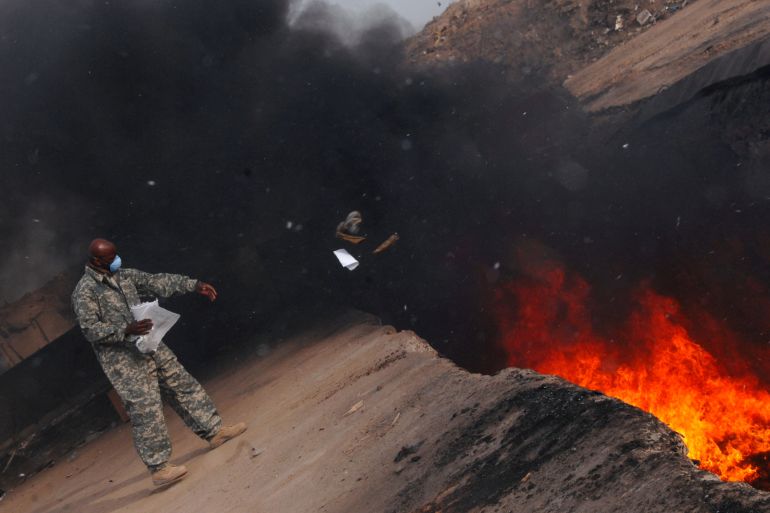 U.S. Air Force personnel toss unserviceable uniform items into a burn pit at Balad Air Base
