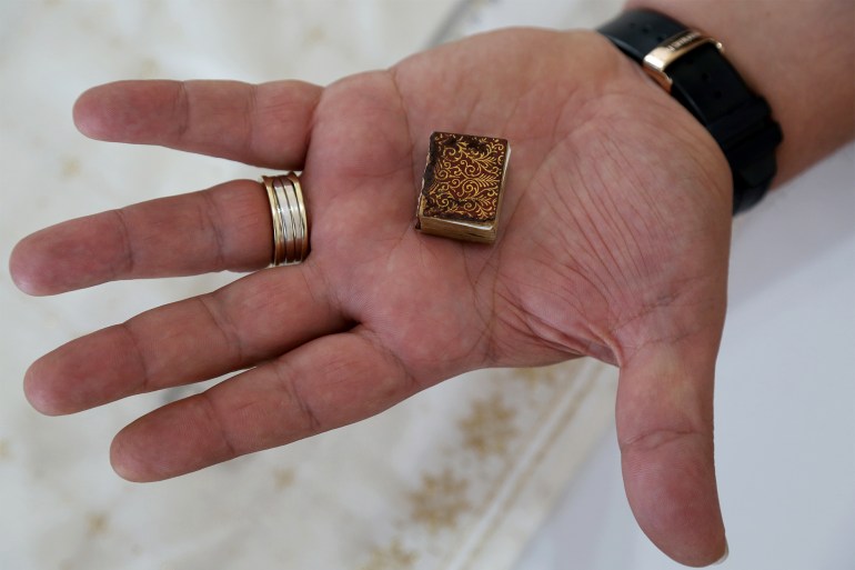 TOPSHOT - Mario Prushi holds in his hand one of the smallest Koran (Islam's holy book), of a postage-stamp size with a cover crafted from gold embroidered velvet, in Tirana, Albania, on April 17, 2023. The ritual is always the same. Mario Prushi carefully washes his hands and face before kissing and pressing one of the world’s smallest Korans to his forehead. For generations, the postage-stamp sized book has been passed down in his family -- surviving authoritarian governments, war, and the perils of time. (Photo by Adnan Beci / AFP)