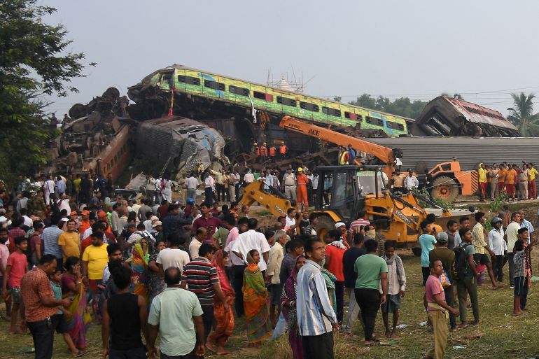 People stand next to damaged coaches after two passenger trains collided in Balasore