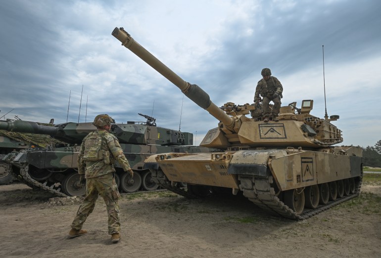 NOWA DEBA, POLAND - MAY 06, 2023: American soldiers are seen next to M1A2 Abrams tank during a high-intensity training session at the Nowa Deba training ground on May 06, 2023 in Nowa Deba, Poland. Anakonda-23 is the highlight of the Polish Army's training calendar this year. Soldiers from various units, including counterparts from the US, Romania, and Slovenia, will collaborate to achieve military excellence using advanced equipment like F-16s, helicopters, missiles, and mortars. (Photo by Artur Widak/NurPhoto via Getty Images)