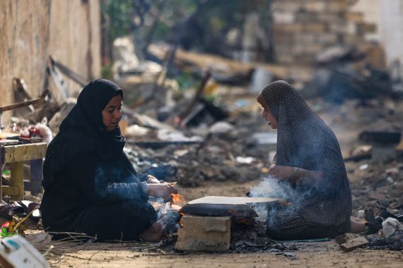 Palestinian women bake on wood fire outside their damaged homes in the Khezaa district on the outskirts of the southern Gaza Strip city of Khan Yunis, following weeks of Israeli bombardment, as a truce between Israel and Hamas entered its second day on November 25, 2023. - Hamas is expected to release another 14 Israeli hostages in exchange for 42 Palestinian prisoners on November 25, as part of a four-day truce in their seven-week war. (Photo by MAHMUD HAMS / AFP)