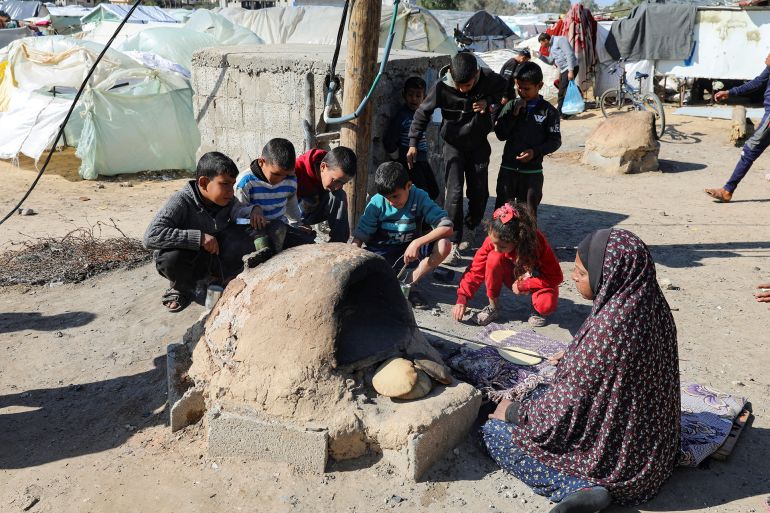 A Palestinian woman bakes bread as children sit next to her, while Gaza residents face crisis levels of hunger and soaring malnutrition, in Khan Younis in the southern Gaza Strip January 24, 2024. REUTERS/Arafat Barbakh