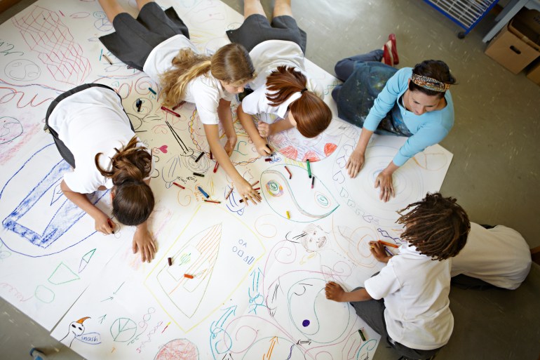 Group of children, aged 10 and 11, working together on a large drawing in a school art class