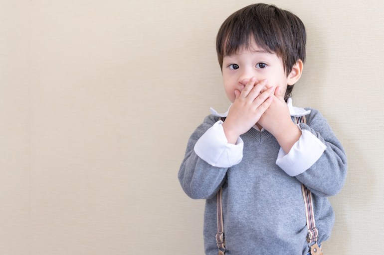 Portrait asian boy standing and used two hands closed his mouth and looking to camera on cream color background