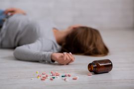 Young woman committing suicide by overdosing on pills, focus on bottle of tablets scattered on floor. Depression and drug overuse, mental breakdown or PTSD problem concept