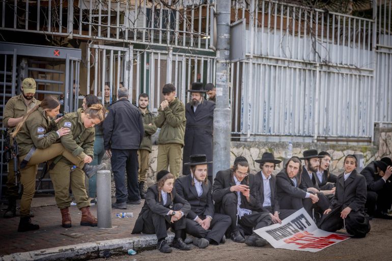 Ultra-Orthodox men after clashes during a protest outside the army recruitment office in Jerusalem, as a group of male and female soldiers stand behind them, March 4, 2024 credit : (Chaim Goldberg/Flash90)