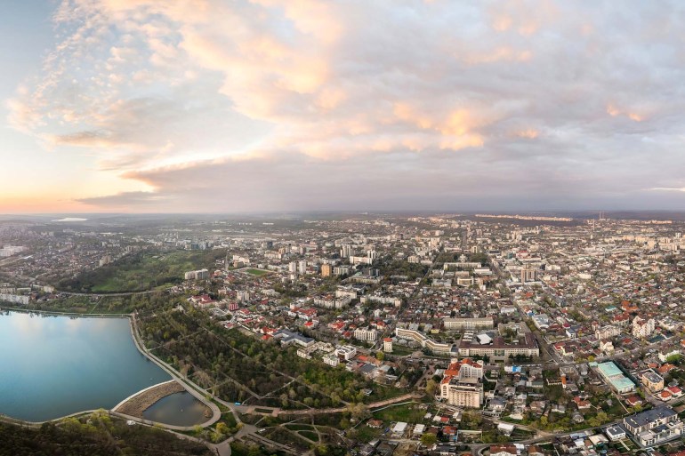 Aerial drone panoramic view of Chisinau at sunset, Moldova. Downtown with Valea Morilor park, multiple residential, governmental and office buildings, greenery