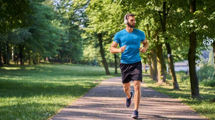 Young man running in park with headphones on sunny summer day; Shutterstock ID 2111195888; purchase_order: aljazeera ; job: ; client: ; other: