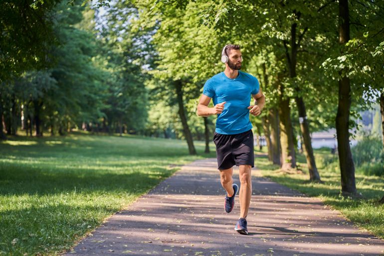 Young man running in park with headphones on sunny summer day; Shutterstock ID 2111195888; purchase_order: aljazeera ; job: ; client: ; other: