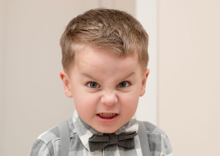 Emotions of anger and anger on a child's face. A small handsome boy, 4 years old, wearing a shirt with a ...