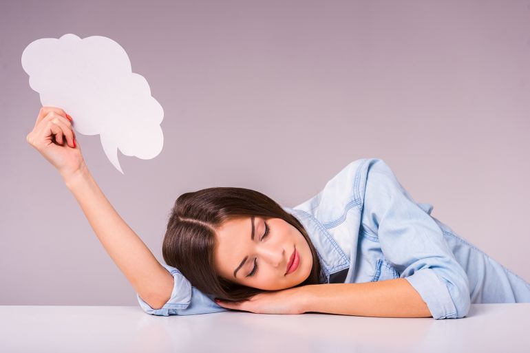 A beautiful young girl sleeping on a table holding a text bubble. Grey background
